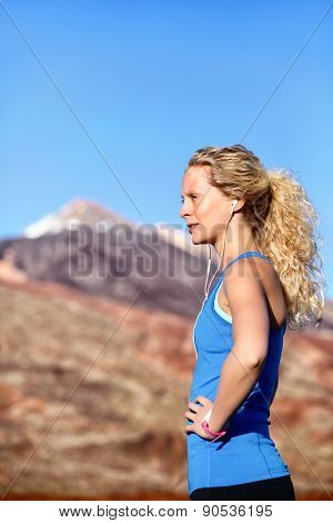 Running earphones - woman runner listening to music in earbuds. Female athlete portrait after running in beautiful nature. Healthy lifestyle concept with beautiful young blonde fitness model.