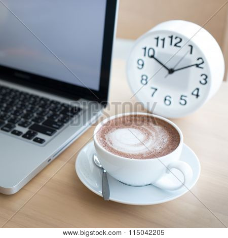 A Cup Of Coffee In A White Cup And Computer Labtop On Mable Table