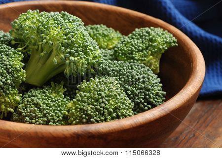 Fresh organic broccoli florets - (uncooked) -  in wooden bowl on rustic table.  Closeup with shallow dof. 