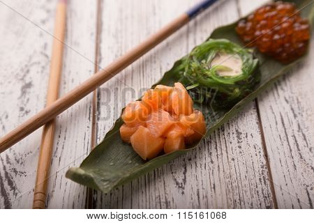 Creative sushi set Japanese food, salmon, chuka salad and caviar on a piece of bamboo