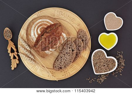 Rustic homemade rye bread on wooden board with wheat sheaths, yeast, olive oil and rye grain in heart shaped dishes and spoon.