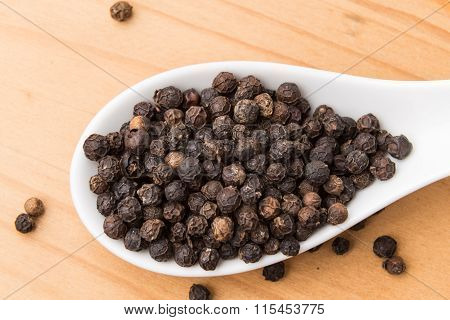 Spoonful Of Black Pepper Corns On Wooden Surface