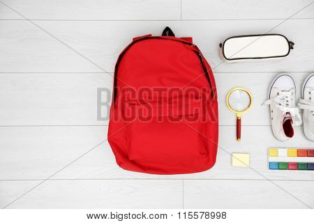 School set with backpack, shoes and supplies on light wooden background
