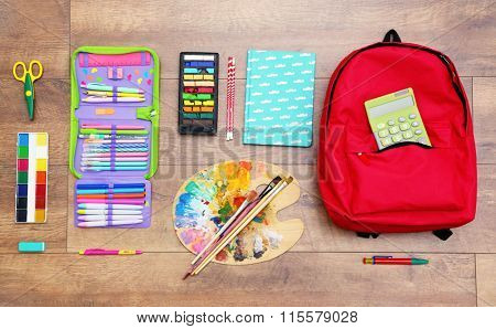 School set with backpack, palette and supplies on wooden background