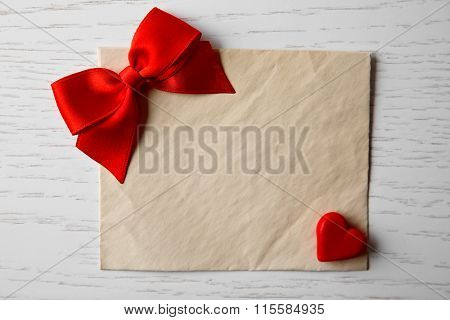 Blank present card with heart and ribbon bow on wooden background