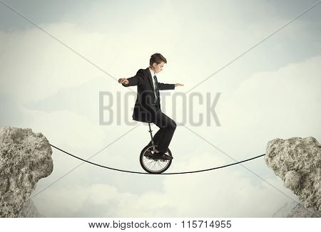 Brave business man riding an mono cycle between cliffs concept