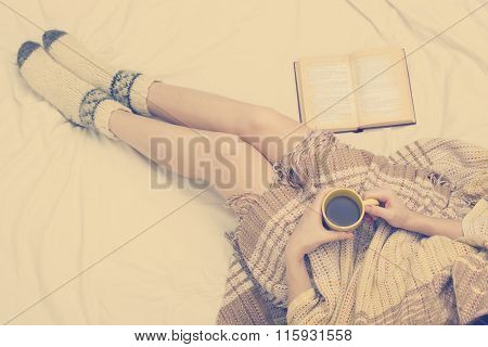 Woman on the bed with old book and cup of coffee in hands, top view point. Copy space for text. Soft