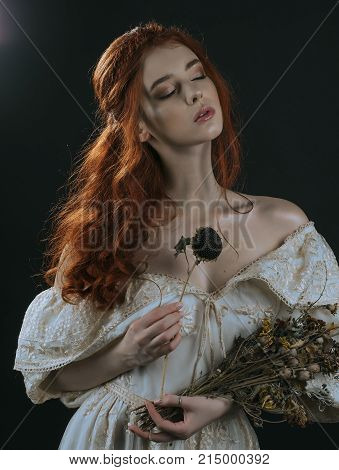 Portrait of a red-haired young woman in a vintage gold dress with a dry bouquet in hands on a black background. A princess. Fairy tale. Art photo