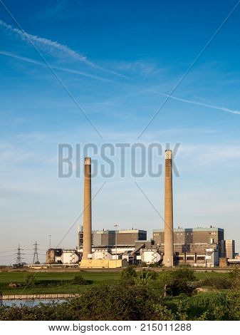 The decommissioned coal powered Tilbury power stations on the north bank of the River Thames with pylons in the background feeding energy into the UK National Grid electricity network.