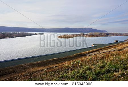 A steep bank to the pier on the Volga River in the Samara region in Russia November water waves. On the river islands which are at home. A barge is sailing along the river. On the other shore Zhugulevskie mountains are lilac. There are clouds in the sky i