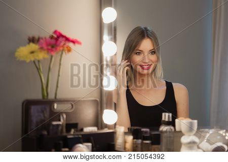 Attractive Blonde Girl Primp At The Mirror With Lamps In The Beauty Studio.