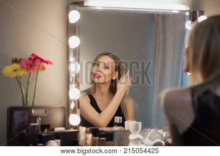Attractive Blonde Girl Primp At The Mirror With Lamps In The Beauty Studio.