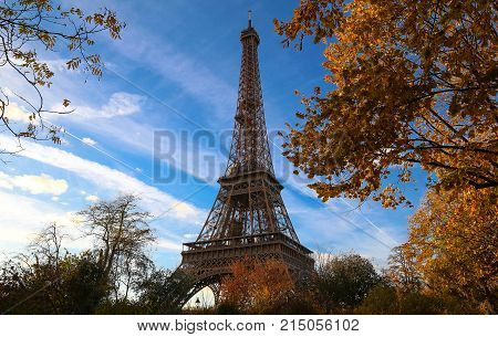 Color fall image of the Eiffel tower in Paris, France, Europe, on a sunny autumn day with blue sky and colorful leaves .