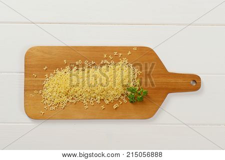 heap of uncooked alphabet pasta on wooden cutting board