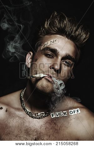 Antisocial behavior, bad habits. Portrait of a bad boy smoking cigarette. Rocker, punk.