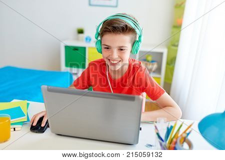 technology, gaming and people concept - boy in headphones playing video game on laptop computer at home