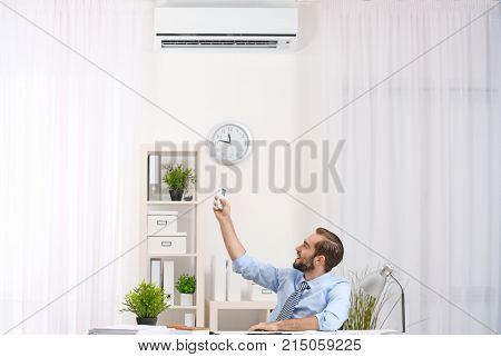 Young man with turning on air conditioner at table in office