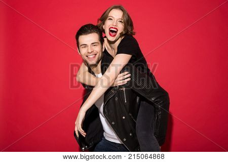 Cheerful young punk couple rejoice together and looking at the camera over red background