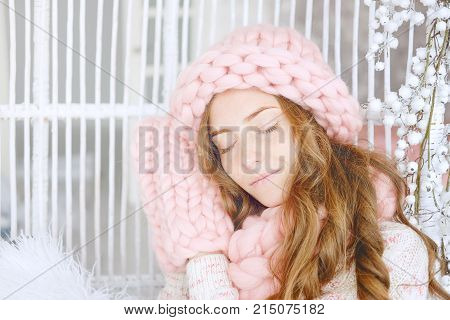 Young woman with red hair and dressed in sweater and knitted pink hat and snood sitting in her favourite chair