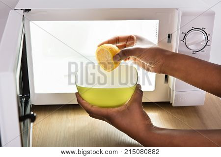 Human Hand Putting Sliced Lemon In Bowl Near Open Microwave