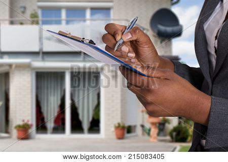 Close-up Of A Person's Hand Filling Document In Front Of House