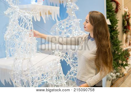 Cheerful customer girl choosing white Christmas decorations.