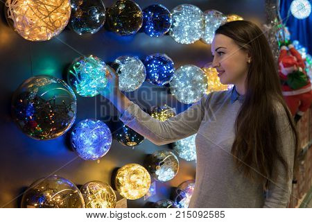 Cheerful happy customer girl choosing Christmas tree decorations - garlands. difficult decision. Various choice