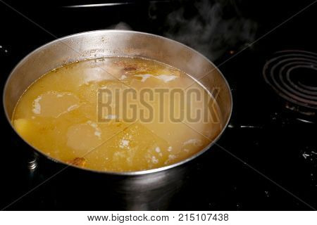 Pork stock simmers in a stock pot on a black stove showing the rising steam.