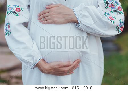 Ukrainian pregnant woman wear traditional embroidered shirt. Location in traditional ukrainian village. Pregnancy concept.