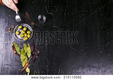 The man eats with a fork olives n dark background
