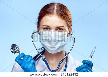 Young beautiful woman in medical mask and robe holds a stethoscope and shrits on a blue background, medicine, doctor.