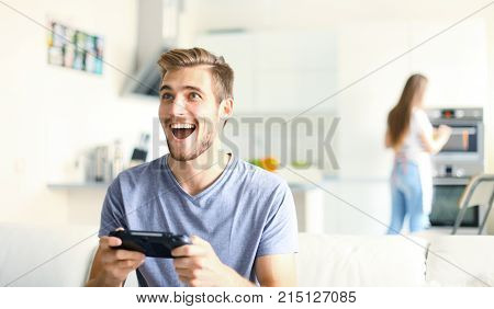 Man playing video games while his girlfriend cooking in the kitchen