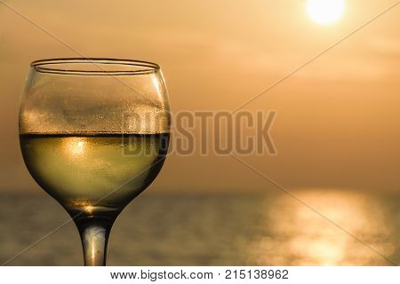 Glass Filled With White Wine Against Sea At Sunset