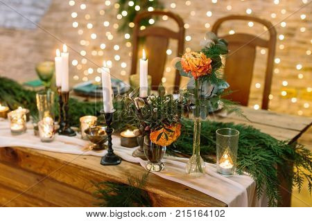 christmas, celebration, design concept. close up of delicate flower, bud of rose in tender orange colour, it is surrounded by lots of candles and leghts, glasses and fuzzy branches of spruce