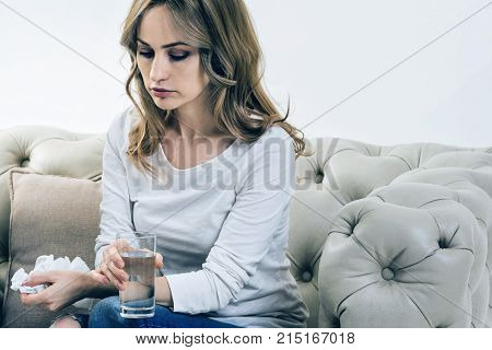 Period of depression. Sad depressed beautiful woman holding crumpled paper tissues and drinking water while coping with depression