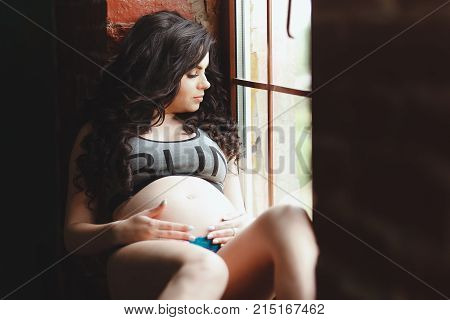 young pregnant woman in lingerie sitting on the window sill