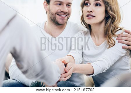 Happy patients. Cheerful positive young woman sitting together with her husband and expressing her gratitude to her therapist while feeling happy