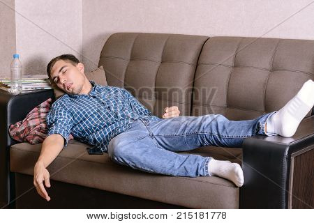 The sleeping young man on the couch in the room tired after work drunk after a party. Fell asleep anyhow