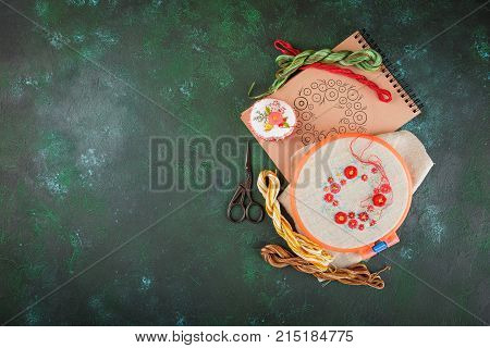 Set with embroidery in the process the embroidery frame linen cloth scheme embroidery thread scissors embroidered knitting head. Top view.