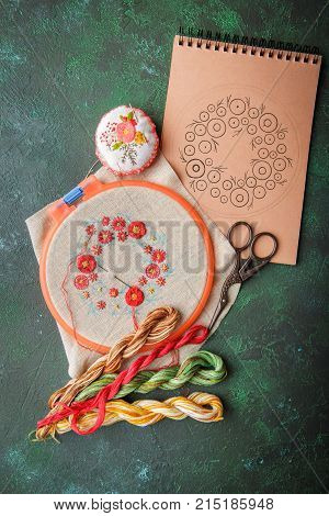 Set with embroidery in the process the embroidery frame linen cloth scheme embroidery thread scissors embroidered knitting head. Top view.