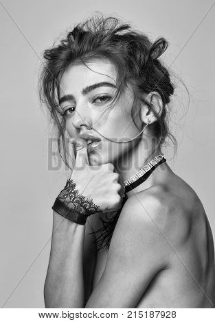 Pretty girl or beautiful woman young cute sexy fashion model with curly hair nose ring and necklace with cuffs poses topless with thumb on lips on grey background
