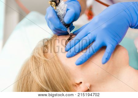 Cosmetologist applying permanent make up on eyebrows. Beautiful woman with smooth young skin sitting in a beautician. A beautician performs modeling permanent eyebrows makings.