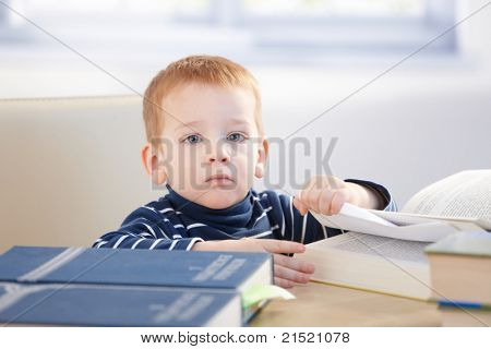 Seriózní malý vědec sedí u stolu, studium encyklopedii.?