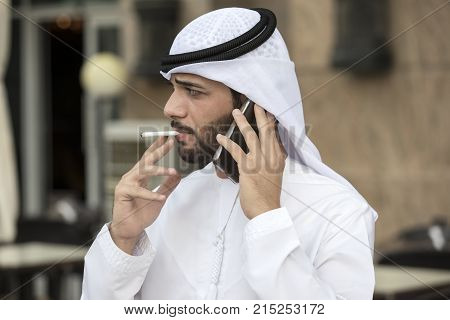 Arab young men smoking a cigar while talking on the phone