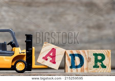 Yellow plastic forklift hold letter A to complete word ADR (Abbreviation of Adverse drug reaction) on wood background