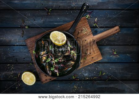 Delicious mussels. Serving on a hot frying pan with herbs spices and lemon on a colored wooden background. Top view.