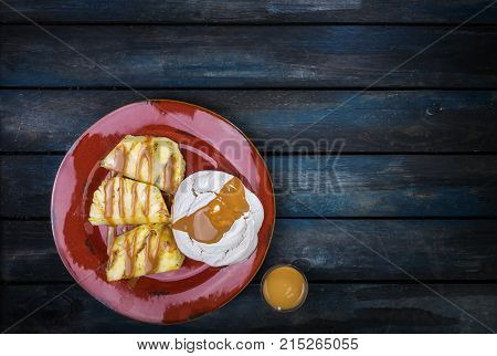 Delicious dessert. Meringue with pineapple and sweetened condensed milk on a colored wooden background. Top view.
