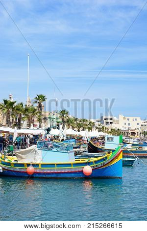 MARSAXLOKK, MALTA - APRIL 1, 2017 - Traditional Maltese Dghajsa fishing boats in the harbour with waterfront buildings and market stalls to the rear Marsaxlokk Malta Europe, April 1, 2017.