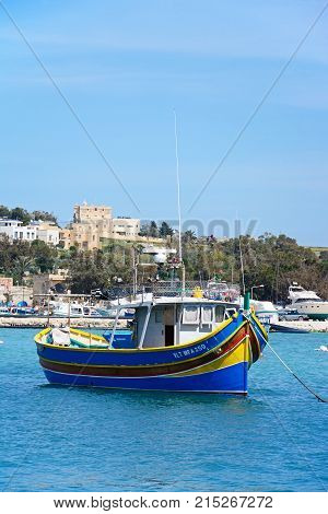 MARSAXLOKK, MALTA - APRIL 1, 2017 - Traditional Maltese Dghajsa fishing boat in the harbour with waterfront buildings to the rear Marsaxlokk Malta Europe, April 1, 2017.
