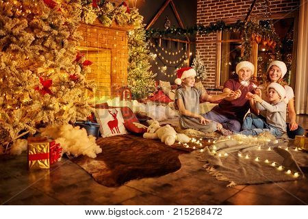 Family with Bengal lights in the room with a Christmas tree and a fireplace on Christmas Day.